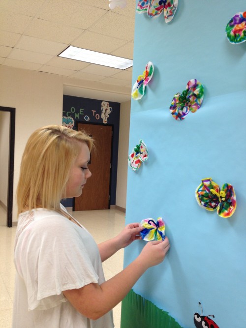 Hannah Suda, Kids’ Corner member and senior, works on one of the bulletin boards outside the Kids’ Corner classroom. She said this was for the week themed Swing into Spring. OLIVIA WEPRICH / PHOTO