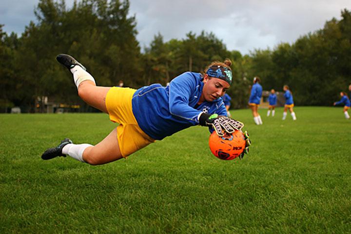 Goalkeeper and senior Nicole Vohs warms up for a game with her teammates in the background. While on the same team, goalkeepers go through an entirely different warm up than the rest of their teammates. Vohs said there is constant pressure on the goalkeeper during the game. Even though she may be inactive for large amounts of time, the one moment that they need to come up with a big save, they have to be ready.