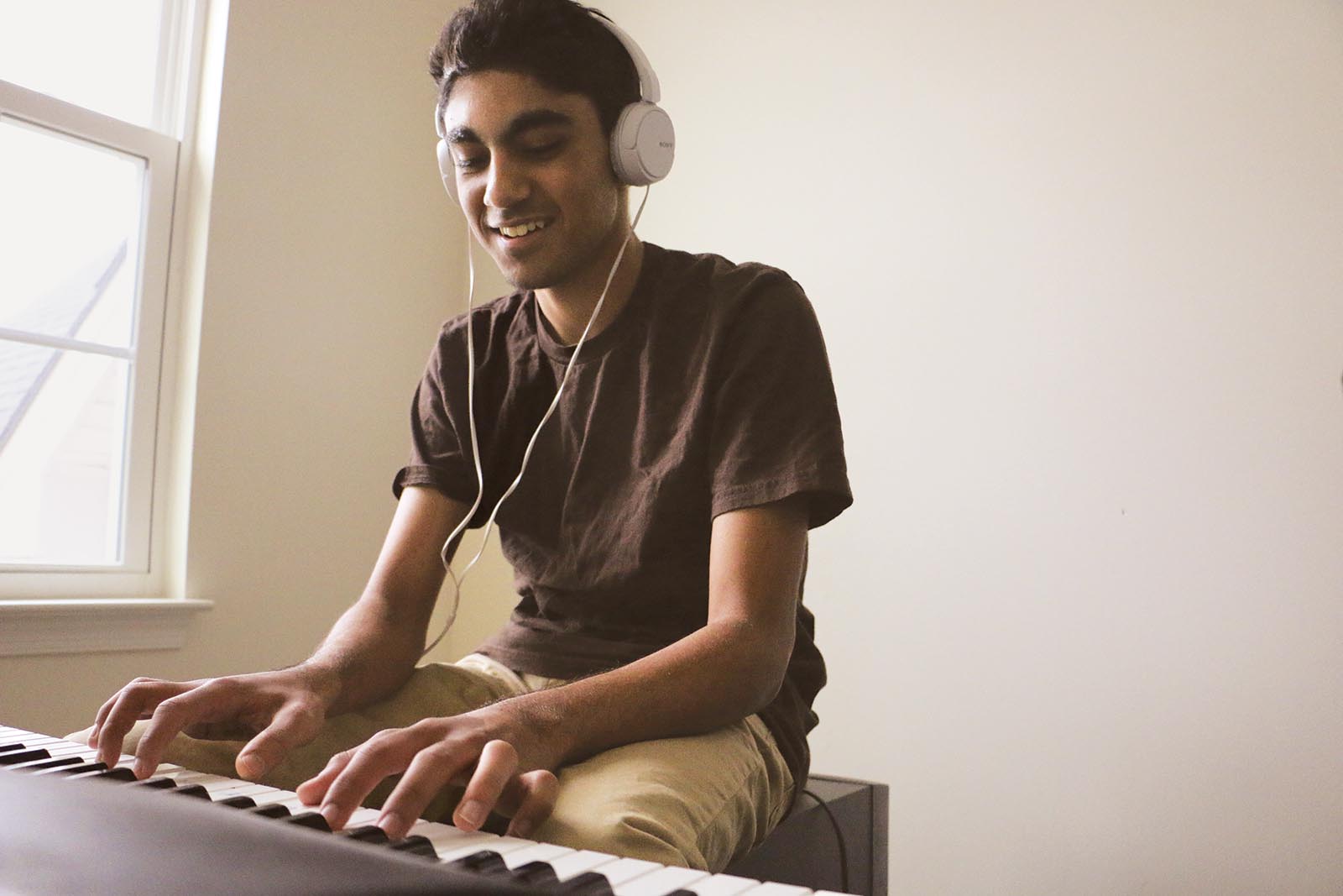 Magesh plays piano while wearing headphones.