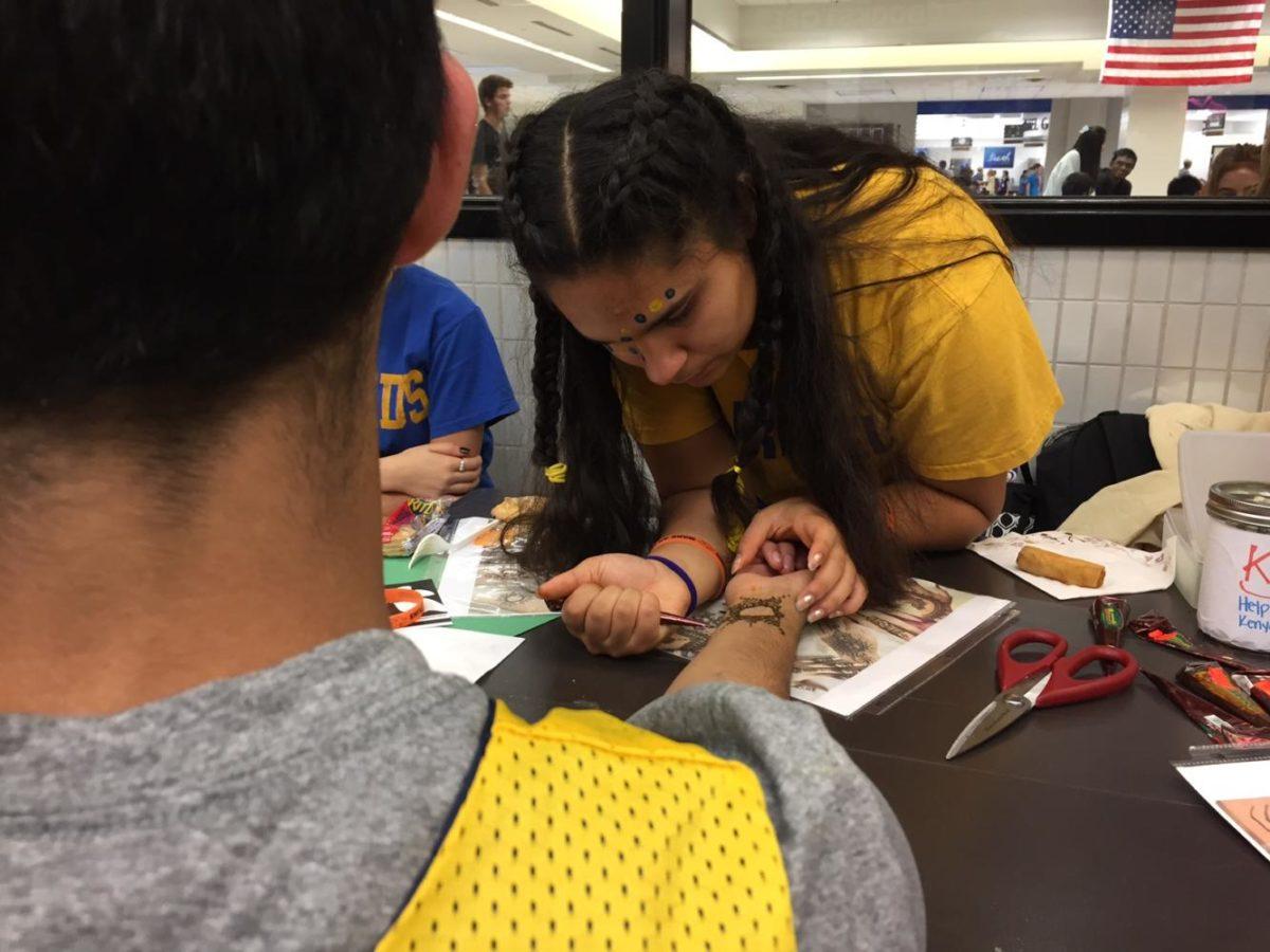  Mayil Bhat, Kenya Club member and junior, applies henna ink on a CHS student to raise money at the Kenya Club Homecoming booth. Mandeep Dhillon, Kenya Club president and junior, said the club will continue fundraise in the future to support the education of Kenyan orphans. 
