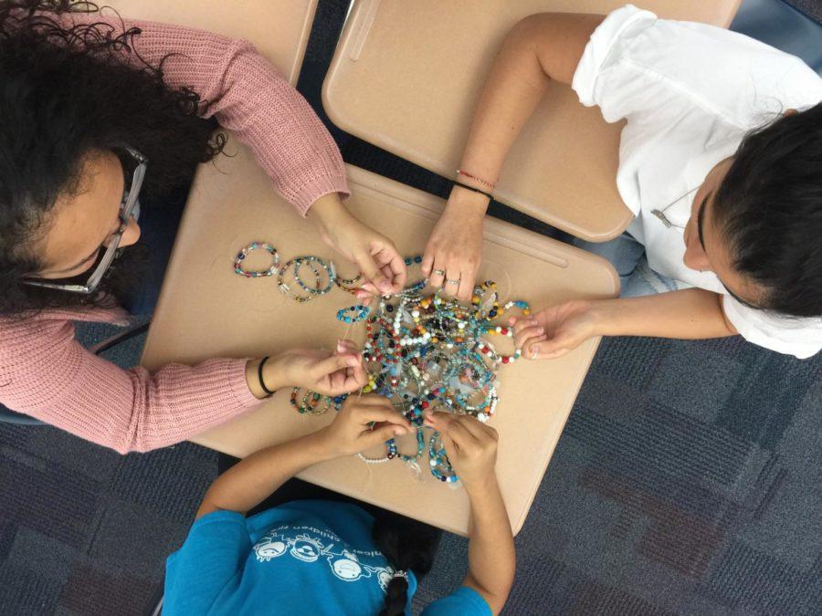 Juniors Mandeep Dhillon, Isabella Yallapragada, and Shubhi Sinha (clockwise from top left) make bracelets as part of a Kenya Club and UNICEF initiative. The leaders plan on selling them for five dollars each to contribute to both of their causes.