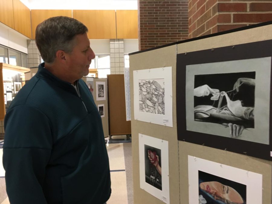 Principal Tom Harmas looks at an art piece in the art show. Harmas said currently he is working on coordinating a counseling survey to assess mental health among students and brainstorming ways to prevent a locker shortage next year despite an influx of students. 