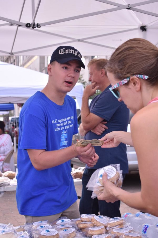 Caiden Wetherald, No Label at the Table Food Co. employee and junior, takes money from a customer at the farmer’s market. According to Shelly Henley, owner and founder of No Label at the Table Food Co., the bakery’s mission is to provide job skills training for people on the autism spectrum. 