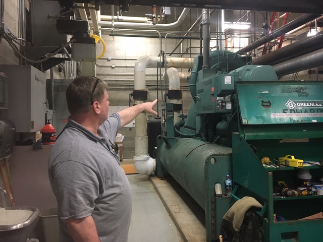  Maintenance worker Fred Napier gestures at one of this school’s chillers. The maintenance department is continuing to work on the chillers with help from Edward’s Electrical and Mechanical to ensure that the school stays at a comfortable temperature. 