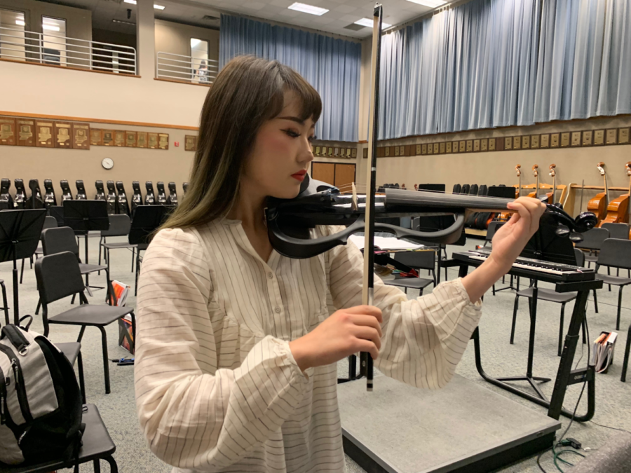 While she plays the electric violin, Jiwon Yu, the club’s president and senior, debates if this is one of the possible new choices of music for the concert for the week of Dec. 12. Yu said, “We will be focusing on sightreading and getting to know the rhythm of the music at our first meeting.”