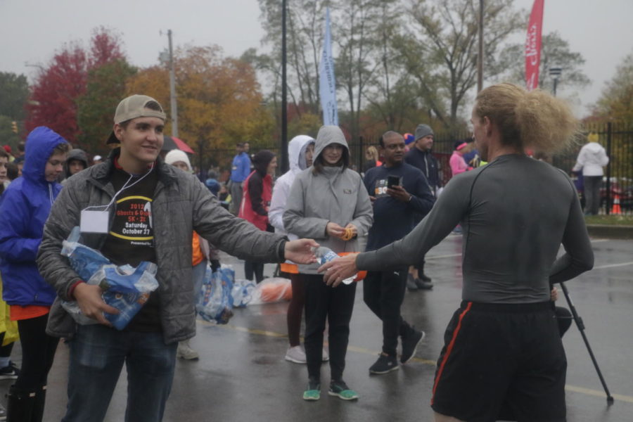  A student volunteer congratulates and hands a water bottle to a runner after he finishes the 5k race. After finishing, all 5k racers were offered a water bottle and a Ghosts and Goblins wristband by volunteers.