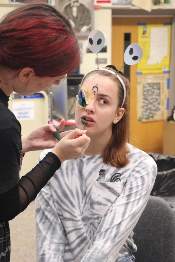 Senior Hannah Smith puts green liquid lipstick on senior Sara Stockholm to finish her alien look for Cheerleaders vs. Aliens. The lipstick Smith is using is by Jeffree Star, famous for his colorful lipsticks shades and eyeshadow palettes. 