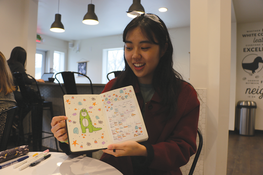 Senior Jaehee Kim shows her friends a spread in her bullet journal. Kim said she likes to make paper crafts and prefers to decorate her bullet journal with paper rather than calligraphy.