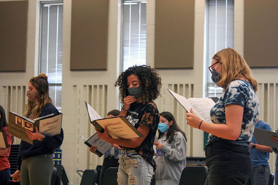 Seniors Abby Mysogland, Gabriella Zalam, and and Cora Lucas look at their sheet music as they sing along
to the music. The entire choir is required to keep
their masks on while they sing and maintain social distancing. 