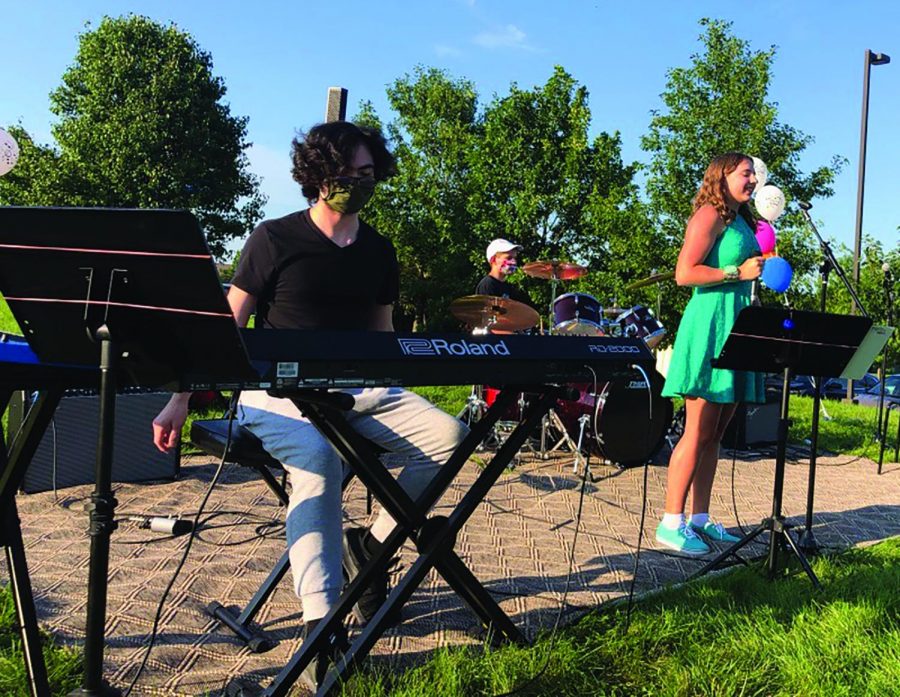 Mackenzie Edwards (right), lead singer of band Lightning in a Bottle and sophomore, sings outside with accompaniment from her bandmates. Edwards said that being involved with the band has allowed her to interact with a vibrant community and share music with others.