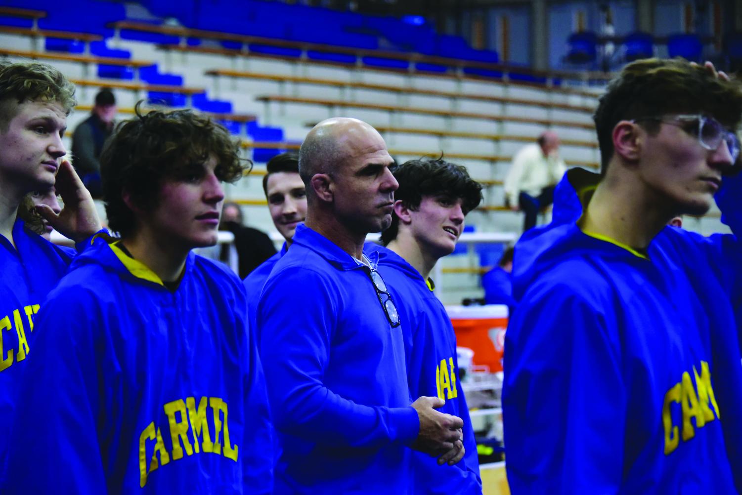 Wrestling coach Ed Pendoski (center) stands amidst wrestlers as he watches a wrestling match. Pendoski said that along with building connections with athletes, an important part of his job as a coach is to provide athletes with experiences that help them grow.