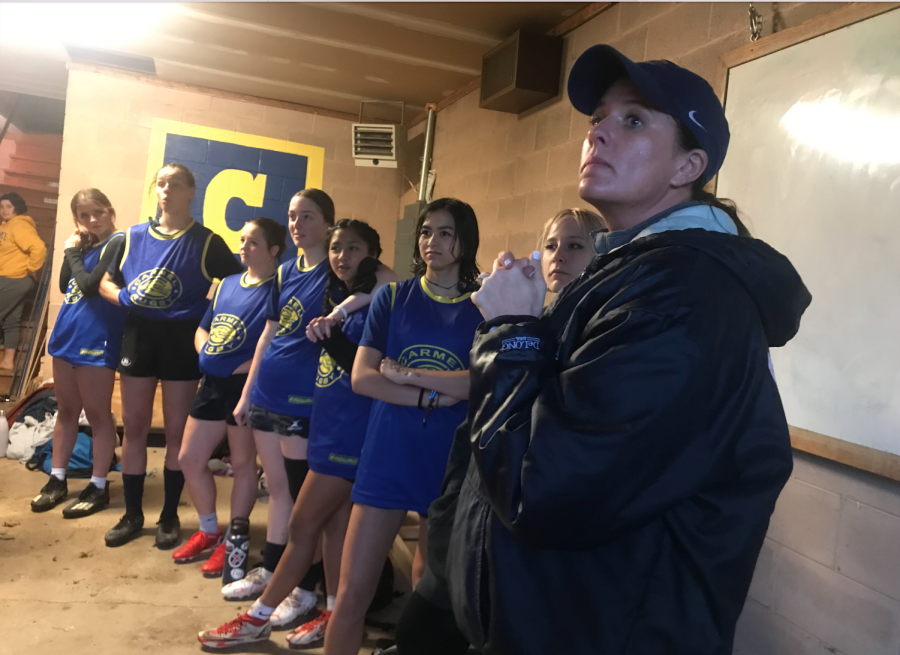Coach Kelly Romano stands before some members of the girls rugby team, listening attentively to another member of the team talk.