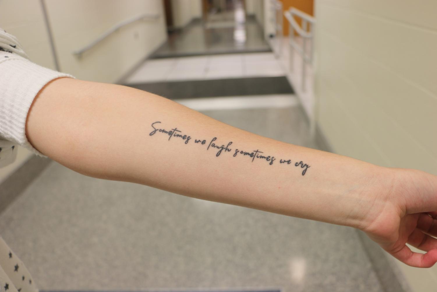 Junior Caroline Miller displays the tattoo on her arm. The tattoo reads, Sometimes we laugh sometimes we cry.