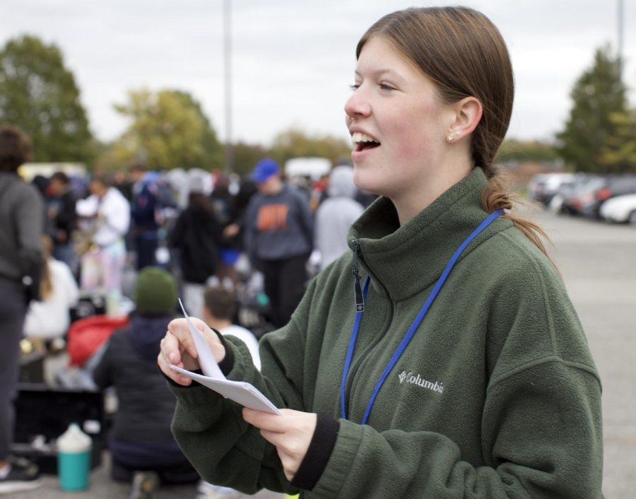Marching Band senior Ava Kuznarsky passes out dot sheets to her section during an after school practice on Oct. 18, 2022. The recent practices were particularly difficult as the band entered the competition portion of their season. “Especially with the New York trip this year, stakes are higher and the responsibilities of helping younger members reach our standards are placed onto us as the most experienced members,” Kuznarsky said.