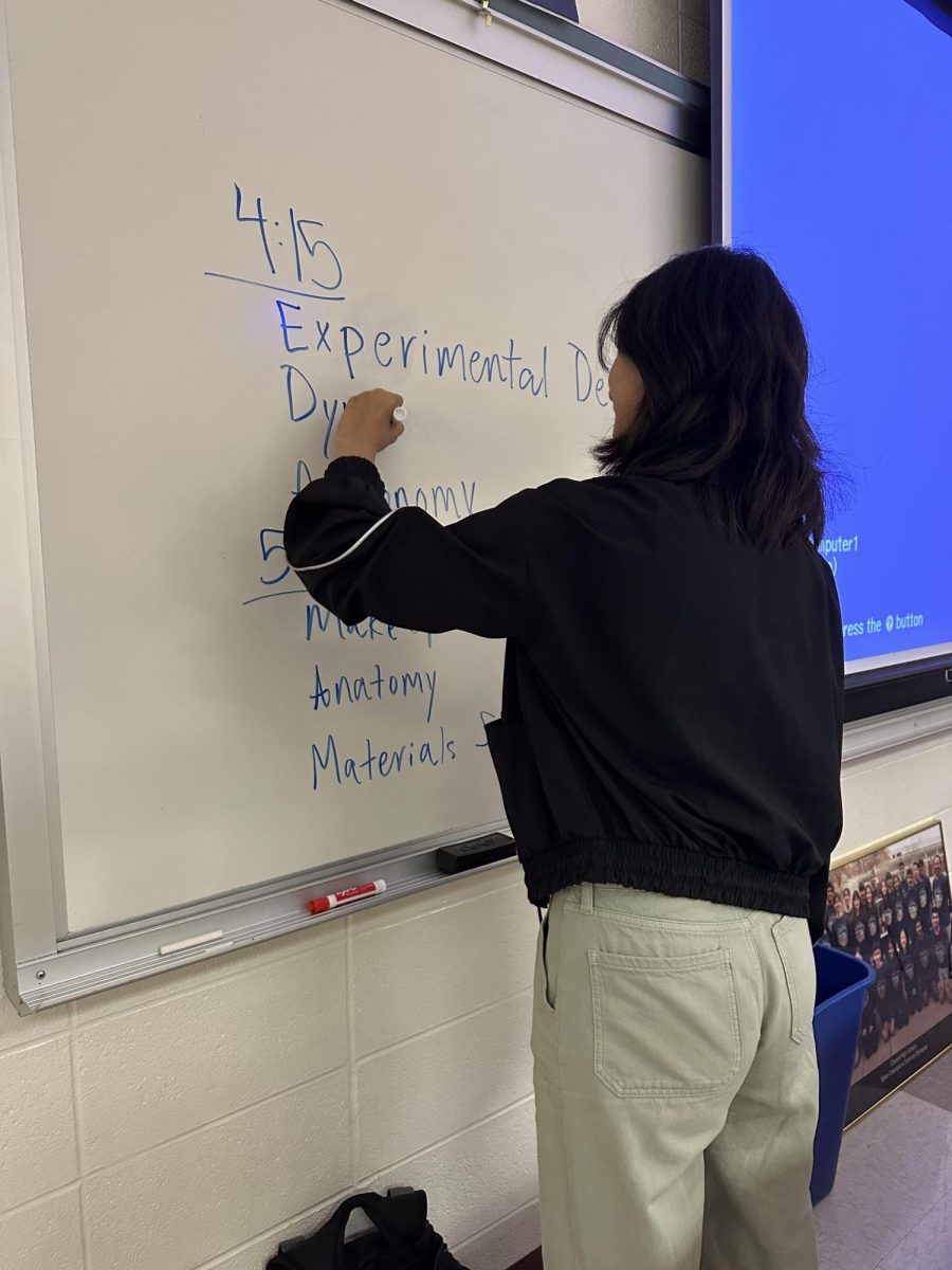 Science Olympiad officer Ava Liao writes the event workshops on the board. Liao said she enjoys leading workshops because she gets to teach and interact with students.  