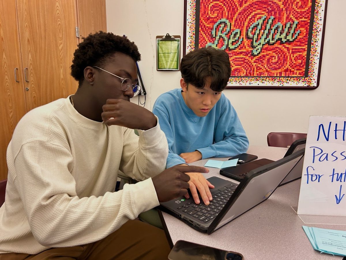 Justin Macharia, NHS president and senior, teaches senior Kellen Gong how to sign up for TVC volunteer opportunities. 