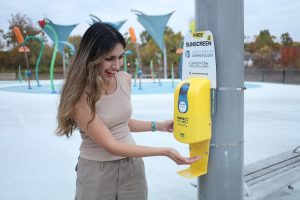 Junior Sophia Tahir tries out the new sunscreen dispensers at the Westermeier Commons Playground and Splash Pad on October 25th. 2024. Carmel Clay Parks had only recently implemented these in order to help and raise awareness about sun protection. “Sunscreen is a need to protect against skin cancer,” said Tahir.