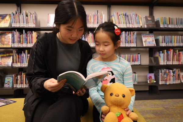 Sophomore Stephanie Tan reads to a young girl at the CCPL after donating toys on Nov. 23. Tan said, “I enjoy being a mentor to kids because I feel like having someone to teach you things and guide you is important.” 