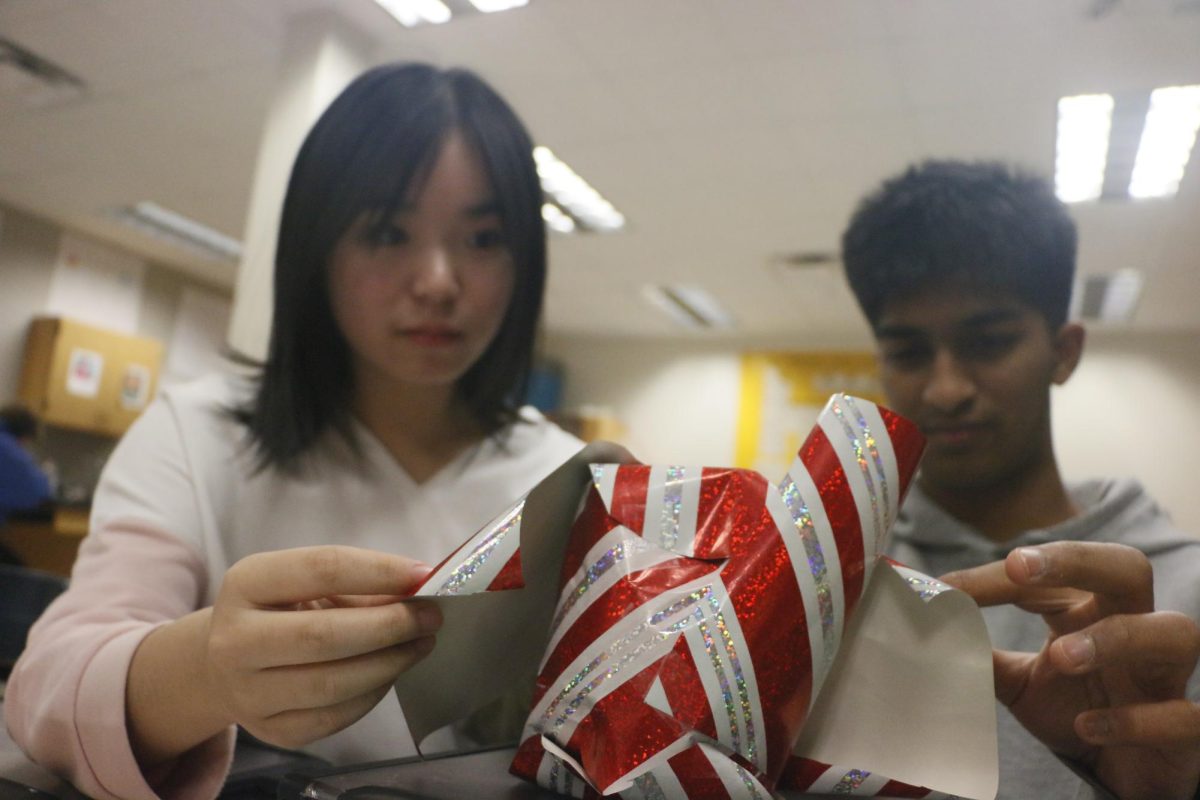 Sophomores Lorie Cai and Nikhil Muragan wrap a snow globe that Nikhil plans to gift one of his friends for Christmas in SSRT on Dec. 2. Murugan decided to participate in a Secret Santa event because he thought it would be a valuable bonding experience with his friends. During the holiday season, many extracurricular classes and individual friend groups engage in gift exchanges.